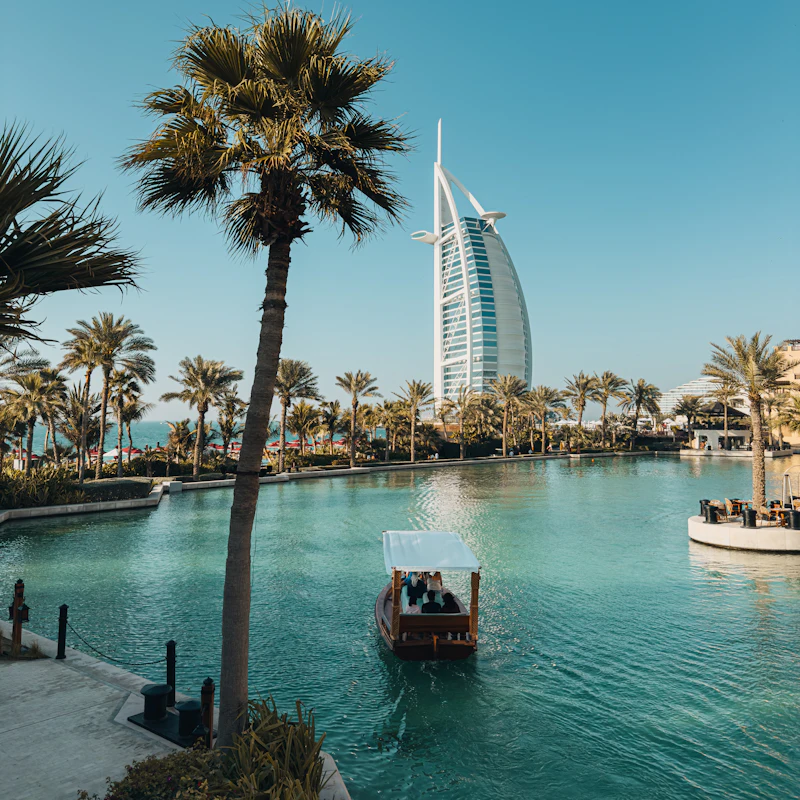 La Burj Al Arab vue depuis un canal bordé de palmiers, avec une abra traditionnelle