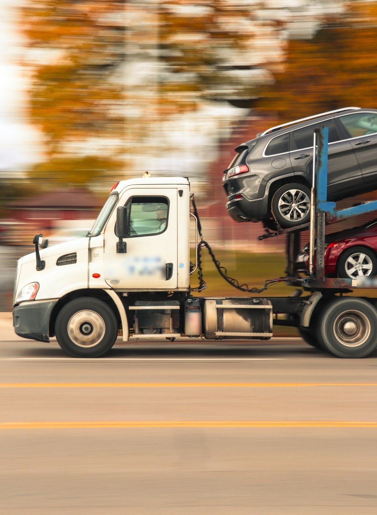 Un camion porte-voitures sur la route, chargé d’un SUV et d’une voiture