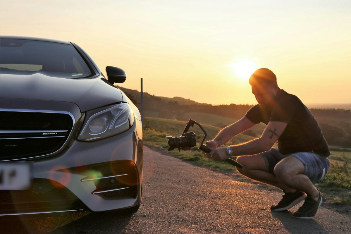 Un vidéaste filme une voiture avec une caméra sur stabilisateur, au coucher du soleil