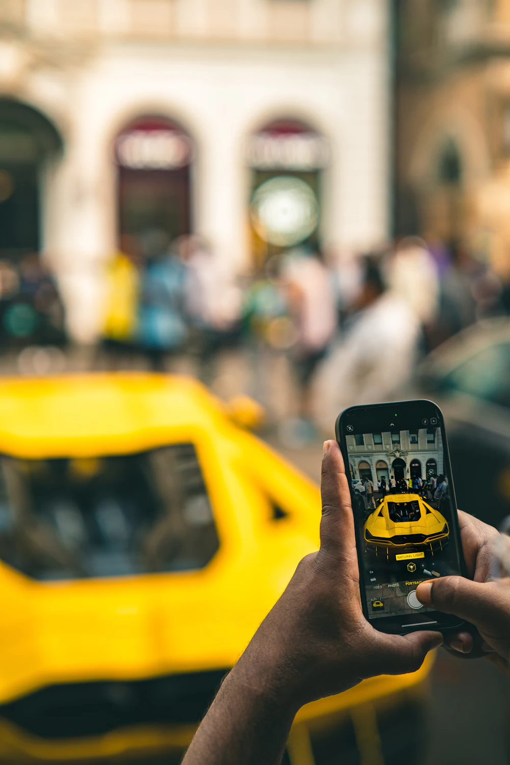 Une main photographie une voiture de sport jaune avec un smartphone