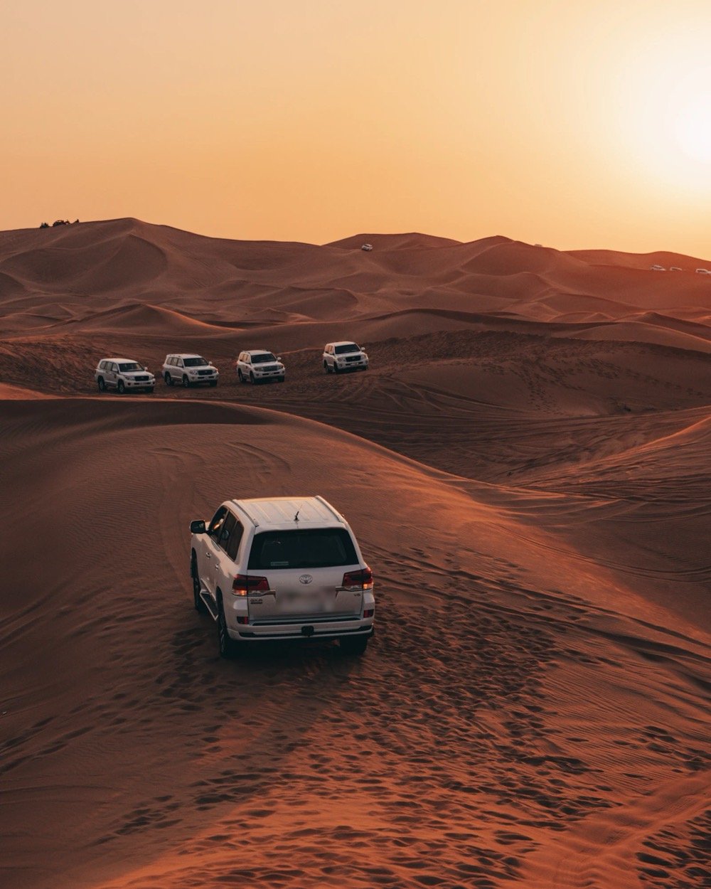 Un 4x4 blanc traverse les dunes du désert près de Dubaï au coucher du soleil