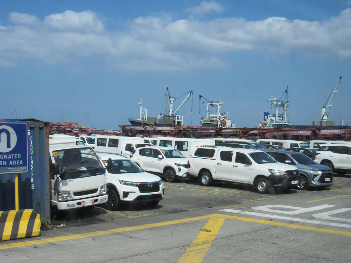 Rangées de véhicules blancs garés sur un terminal portuaire, près de navires de charge
